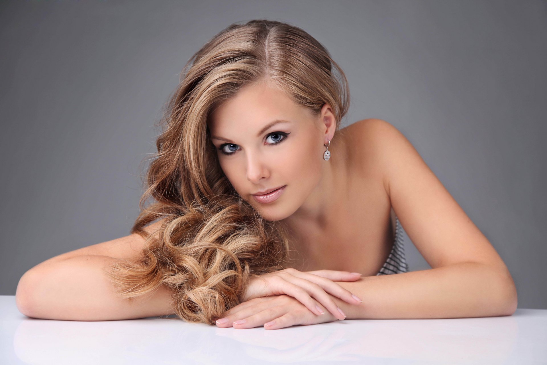 girl blonde face view hair curls earrings make-up of the arrow hands gray background