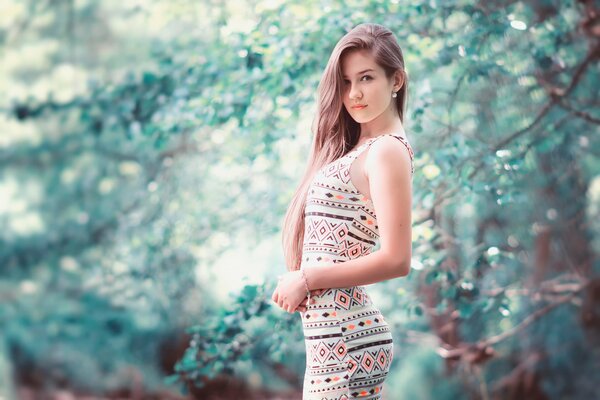 A girl in a dress stands against the background of a forest